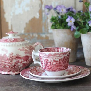 Puede incluir: Un juego de té vintage con un patrón floral rosa y blanco. El juego incluye una tetera, una taza de té y un platillo. La taza de té y el platillo tienen un patrón floral a juego. La tetera tiene una tapa con un pomo en la parte superior. El juego de té está sobre una mesa de madera.