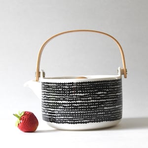 Può includere: Una teiera in ceramica con un motivo bianco e nero e un manico in legno. La teiera ha un corpo rotondo.