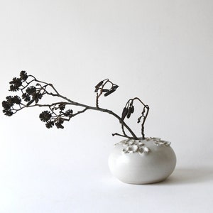 May include: A white ceramic vase with a textured surface and a single branch of dried flowers.