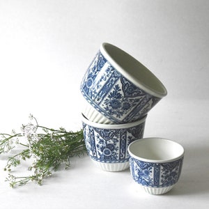 Peut inclure: Quatre ramequins en céramique blanche avec un motif floral et géométrique bleu. Les ramequins sont empilés, avec un légèrement à l'écart. Le motif comprend des fleurs, des feuilles et des formes géométriques. Les ramequins ont un extérieur cannelé.