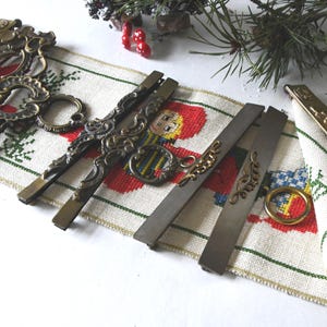 May include: Antique brass drawer pulls and decorative hardware pieces arranged on a Christmas-themed embroidered runner. The hardware includes ornate handles and pulls with intricate scrollwork and a vintage aesthetic.