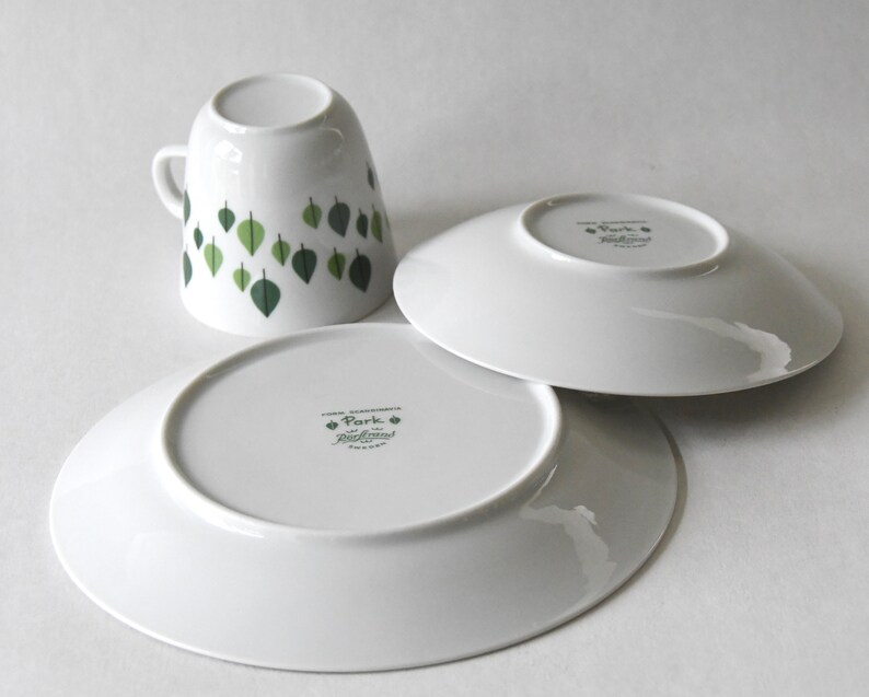 Puede incluir: Juego de taza y platillos de cer&aacute;mica blanca con dise&ntilde;o de hojas. La taza presenta hojas verdes, y los platillos son blancos. El juego es de la colecci&oacute;n "Park".