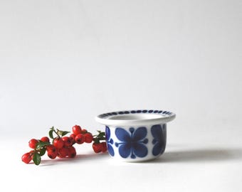 Peut inclure: Un petit coquetier en céramique blanche orné d'un motif floral bleu foncé répétitif sur l'extérieur et d'un bord bleu à pois. Une branche de baies rouge vif avec de petites feuilles vertes est placée juste à côté du coquetier en céramique.