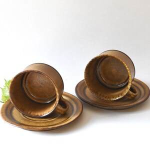 May include: Two brown ceramic coffee cups with matching saucers. The cups are upside down and the saucers are underneath.