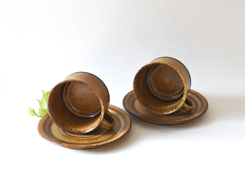 May include: Two brown ceramic coffee cups with matching saucers. The cups are upside down and the saucers are underneath.