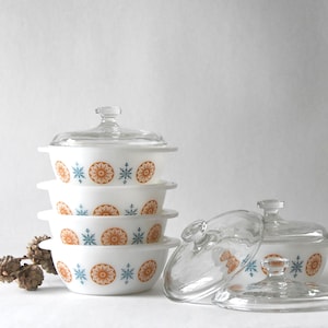 May include: A set of four white glass casserole dishes with lids. The dishes feature a blue and orange snowflake design.