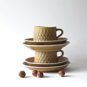 May include: A set of three brown and white ceramic coffee cups and saucers with a geometric pattern. The cups and saucers are stacked on top of each other.