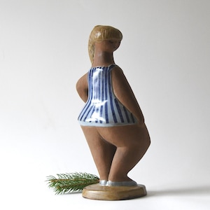 Könnte beinhalten: Keramikfigur einer Frau mit blonden Haaren und einem blau-weiß gestreiften Oberteil. Die Figur steht auf einem runden Sockel. Die Figur hat einen modernen Stil aus der Mitte des Jahrhunderts.