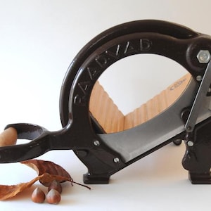 Puede incluir: Un cascanueces de hierro fundido marrón con una base de madera y una cuchilla plateada. El cascanueces está etiquetado como "RAAB & AD".