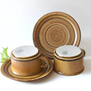 May include: Two brown ceramic coffee cups with matching saucers. The cups have a brown and white glaze and a dark brown rim. The saucers have a brown and white glaze with a dark brown rim.