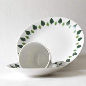 Puede incluir: Un juego de vajilla de cer&aacute;mica blanca con una fuente ovalada grande, una taza de t&eacute; y un platillo. Cada pieza est&aacute; decorada con un borde de dise&ntilde;os de hojas verdes. Ideal para servir comidas o como elementos decorativos.