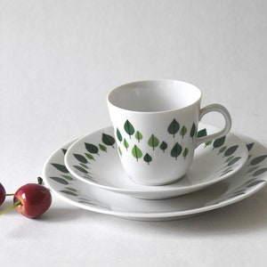 Puede incluir: Juego de t&eacute; de cer&aacute;mica blanca con dise&ntilde;o de hojas verdes. El juego incluye una taza, un platillo y un plato. Dos cerezas rojas en primer plano. Ideal para servir t&eacute; o caf&eacute;.