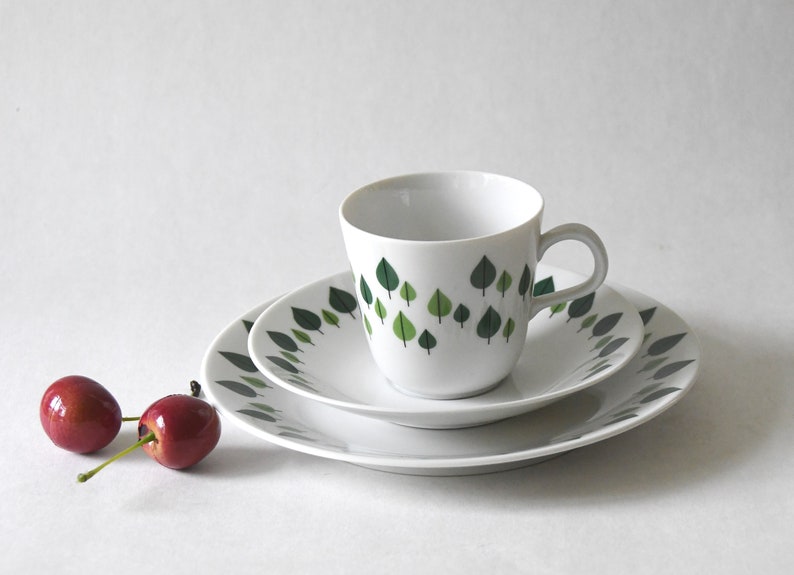 Puede incluir: Juego de t&eacute; de cer&aacute;mica blanca con dise&ntilde;o de hojas verdes. El juego incluye una taza, un platillo y un plato. Dos cerezas rojas en primer plano. Ideal para servir t&eacute; o caf&eacute;.