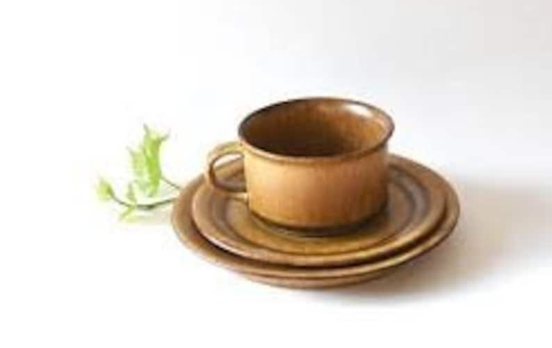 May include: A brown ceramic teacup and saucer set with a textured, striped design. The cup has a handle and the saucer has a slightly raised edge.