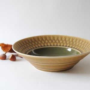 以下が含まれることがあります： 幾何学模様の入った茶色と緑のセラミックボウル。ボウルは上部が少し広がっており、滑らかで光沢のある仕上げになっています。