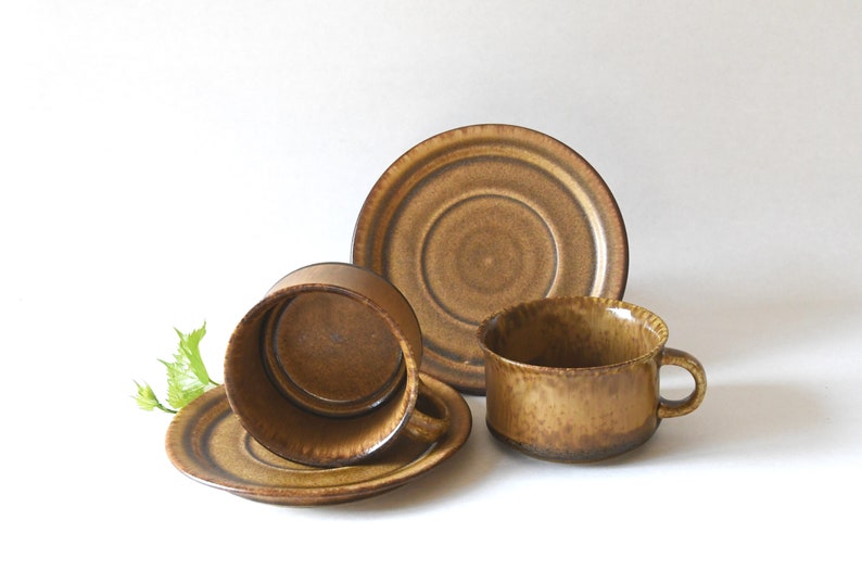 May include: A set of two brown ceramic coffee cups and saucers. The cups and saucers have a mottled brown glaze.