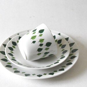 Puede incluir: Un juego de t&eacute; de cer&aacute;mica blanca con una taza y dos platos. El dise&ntilde;o presenta un patr&oacute;n de hojas verdes. La taza est&aacute; inclinada. Los platos est&aacute;n apilados. Ideal para servir t&eacute; o caf&eacute;.