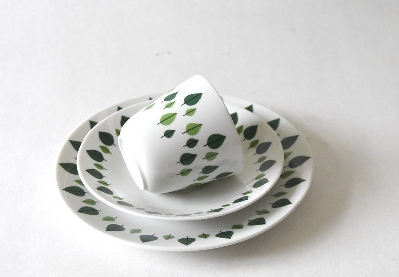 Puede incluir: Un juego de t&eacute; de cer&aacute;mica blanca con una taza y dos platos. El dise&ntilde;o presenta un patr&oacute;n de hojas verdes. La taza est&aacute; inclinada. Los platos est&aacute;n apilados. Ideal para servir t&eacute; o caf&eacute;.