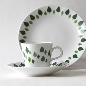 Puede incluir: Un juego de vajilla de cer&aacute;mica blanca con una taza, un platillo y un plato llano. Cada pieza est&aacute; decorada con un patr&oacute;n de hojas verdes. El plato y la taza tienen un borde de hojas, mientras que la taza y el platillo tienen un dise&ntilde;o de hojas dispersas.