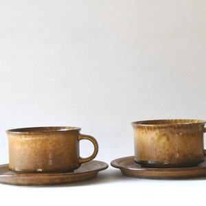 May include: Two brown ceramic teacups with matching saucers. The cups have a textured, speckled glaze.
