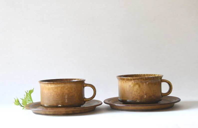 May include: Two brown ceramic teacups with matching saucers. The cups have a textured, speckled glaze.