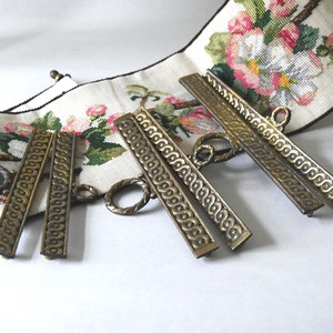 May include: Set of five antique gold-toned metal picture frame hangers with ornate designs. The hangers have a decorative ring at the top for hanging.