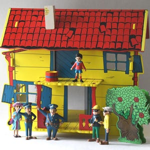 May include: A colorful, vintage toy house with a red roof and yellow walls. Miniature figures of people, including police officers and other characters, stand in front of the house. A tree with red apples is also present.