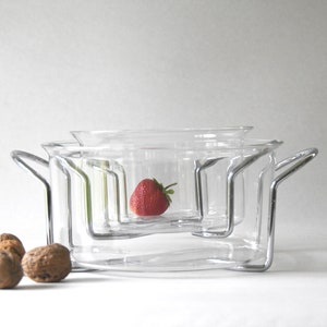 Könnte beinhalten: Ein Satz aus drei klaren Glasschalen mit silbernen Metallgriffen und einem Ständer. Die Schalen sind übereinander gestapelt und eine einzelne Erdbeere liegt in der oberen Schale.