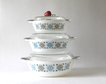 May include: A set of three white ceramic casserole dishes with blue and black geometric patterns. The dishes are stacked on top of each other, with the largest dish on the bottom and the smallest dish on top.