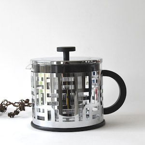 May include: A silver and black tea pot with a geometric design. The pot has a glass body and a black handle.