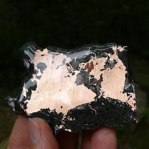 May include: A flat, irregularly shaped piece of dark, glossy black material with a smooth, reflective copper-colored metallic inlay covering a large portion of the surface. The metallic section features organic, jagged edges against the black base.