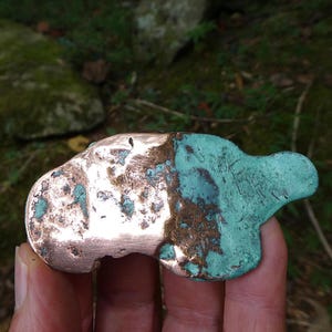 May include: A raw, irregular metal nugget featuring a distinct split appearance. One side displays a polished, shiny copper surface, while the other side is covered in a textured, oxidized patina with a vibrant, matte teal-green coloration.