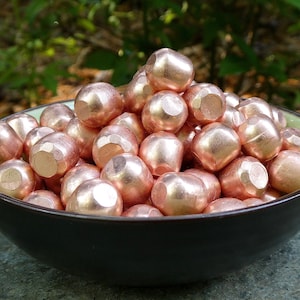 May include: A bowl filled with a large quantity of small, round, copper-colored beads. The beads have a slightly textured surface and are piled high in the bowl.