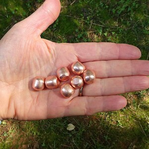 K&ouml;nnte beinhalten: Eine Hand h&auml;lt sechs kupferfarbene Perlen. Die Perlen sind rund und glatt, mit einem leicht gl&auml;nzenden Finish.