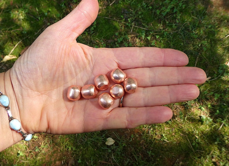 K&ouml;nnte beinhalten: Eine Hand h&auml;lt sechs kupferfarbene Perlen. Die Perlen sind rund und glatt, mit einem leicht gl&auml;nzenden Finish.