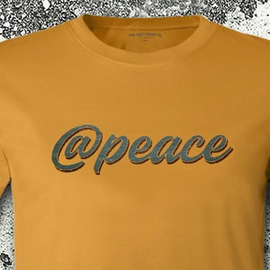 May include: A mustard yellow t-shirt with the text "@peace" in a dark green, stylized font.
