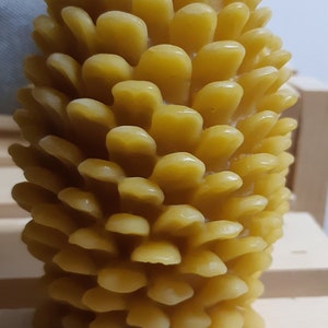 May include: A yellow beeswax candle shaped like a pine cone. The candle has a textured surface and a small wick.