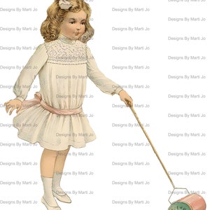 May include: A young girl in a white dress with a pink sash pulls a toy lawnmower with a green and white design. The lawnmower has a pink and white handle and a red and white drum. The girl has a white bow in her hair and is smiling.