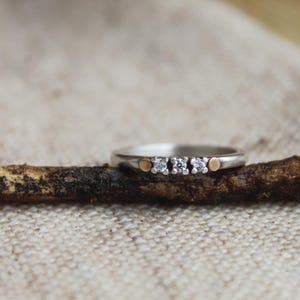 Op de afbeelding: Een zilveren ring met drie kleine diamanten en twee gouden accenten.