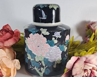 May include: Black ceramic jar with a lid, decorated with pink and purple flowers and green leaves. The jar has a floral design and a bird on the lid.