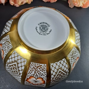May include: A white and gold Caverswall bone china bowl with a geometric pattern and orange floral accents. The bowl is made in England and features the Caverswall logo on the bottom.