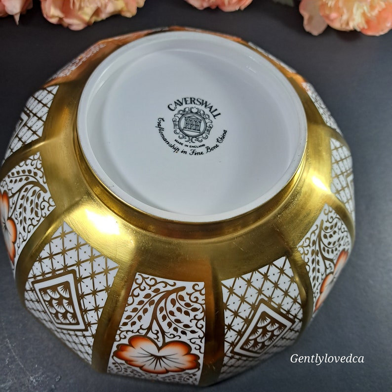 May include: A white and gold Caverswall bone china bowl with a geometric pattern and orange floral accents. The bowl is made in England and features the Caverswall logo on the bottom.