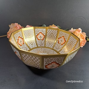 May include: A gold and white octagonal serving bowl with a floral design in orange and red. The bowl has a geometric pattern and is decorated with intricate details.