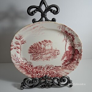 May include: An oval, white ceramic serving platter with a red and white floral design. The center of the platter features a red and white scene of a canal with boats and trees.