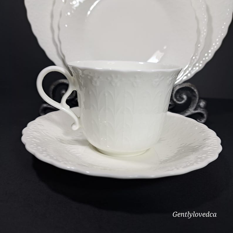 K&ouml;nnte beinhalten: Wei&szlig;es Tee-Set mit Tasse und Untertasse mit einem zarten Blumenmuster. Die Tasse hat einen geschwungenen Henkel und die Untertasse einen gewellten Rand.