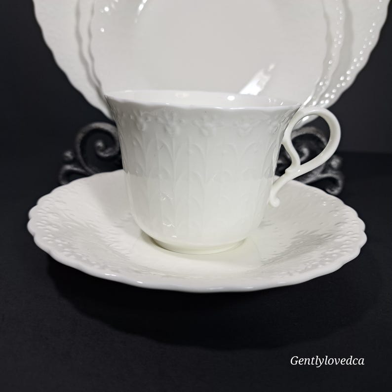 K&ouml;nnte beinhalten: Ein wei&szlig;es Tee-Set mit einem zarten Blumenmuster. Die Tasse hat einen Henkel und die Untertasse einen gewellten Rand.