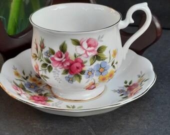 May include: A white teacup and saucer set with a floral pattern. The cup has a gold rim and the saucer has a scalloped edge. The flowers are pink, blue, and yellow.