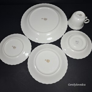 K&ouml;nnte beinhalten: Set aus vier wei&szlig;en Porzellantellern mit gewellten R&auml;ndern. Die Teller haben einen goldenen Rand und eine goldene Inschrift auf der Unterseite, die "Bone China" und "Made in Japan" lautet.