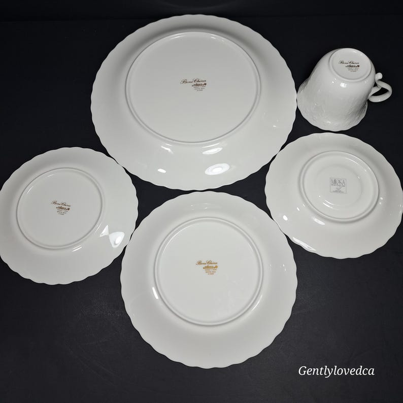 K&ouml;nnte beinhalten: Set aus vier wei&szlig;en Porzellantellern mit gewellten R&auml;ndern. Die Teller haben einen goldenen Rand und eine goldene Inschrift auf der Unterseite, die "Bone China" und "Made in Japan" lautet.