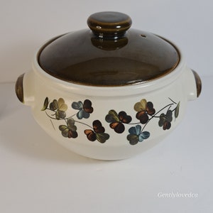 May include: A white ceramic casserole dish with a brown lid. The dish is decorated with a green shamrock pattern.
